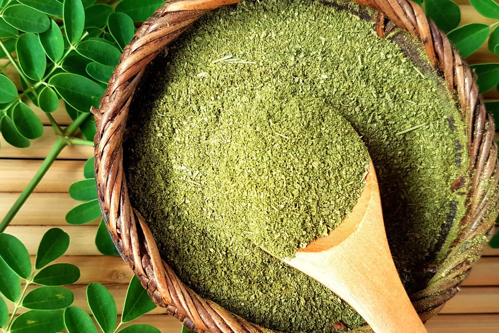 Fresh moringa leaves surrounding a bowl of bright green moringa leaf powder